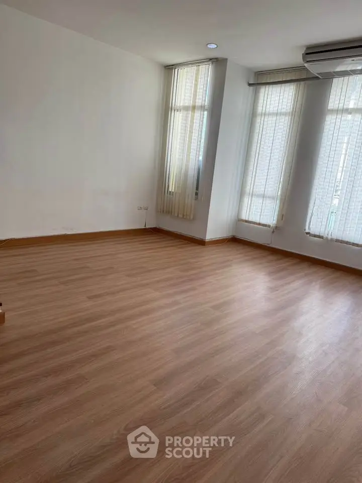 Spacious empty room with wooden flooring and large windows, perfect for customization.