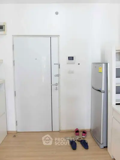 Modern apartment entrance with sleek white door and compact refrigerator.