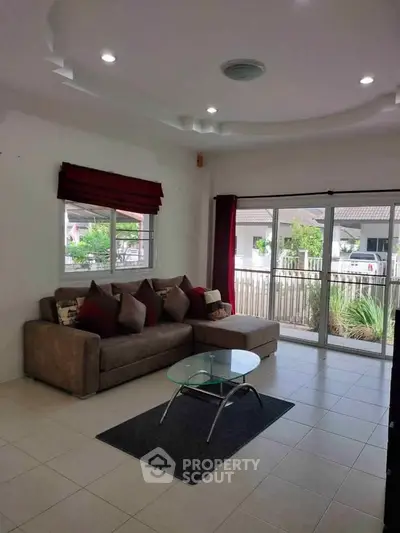 Spacious living room with modern sofa and glass coffee table, featuring large windows and garden view.