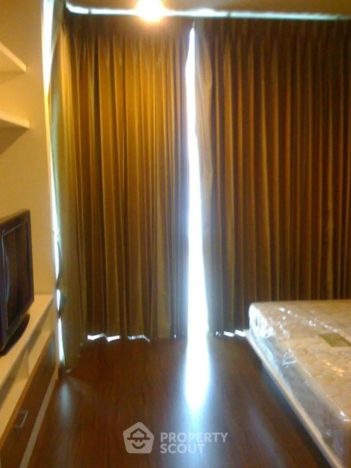 Cozy bedroom with floor-to-ceiling curtains and wooden flooring, featuring a TV and a comfortable bed.