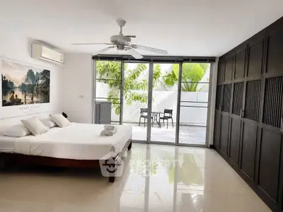 Spacious bedroom with large windows and garden view, featuring modern decor and ample natural light.
