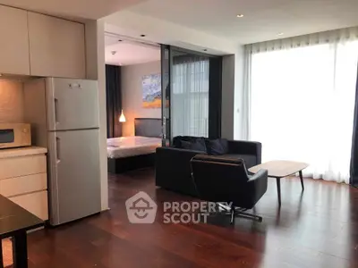 Modern open-plan living room with sleek kitchen and cozy bedroom area, featuring stylish furniture and natural light.