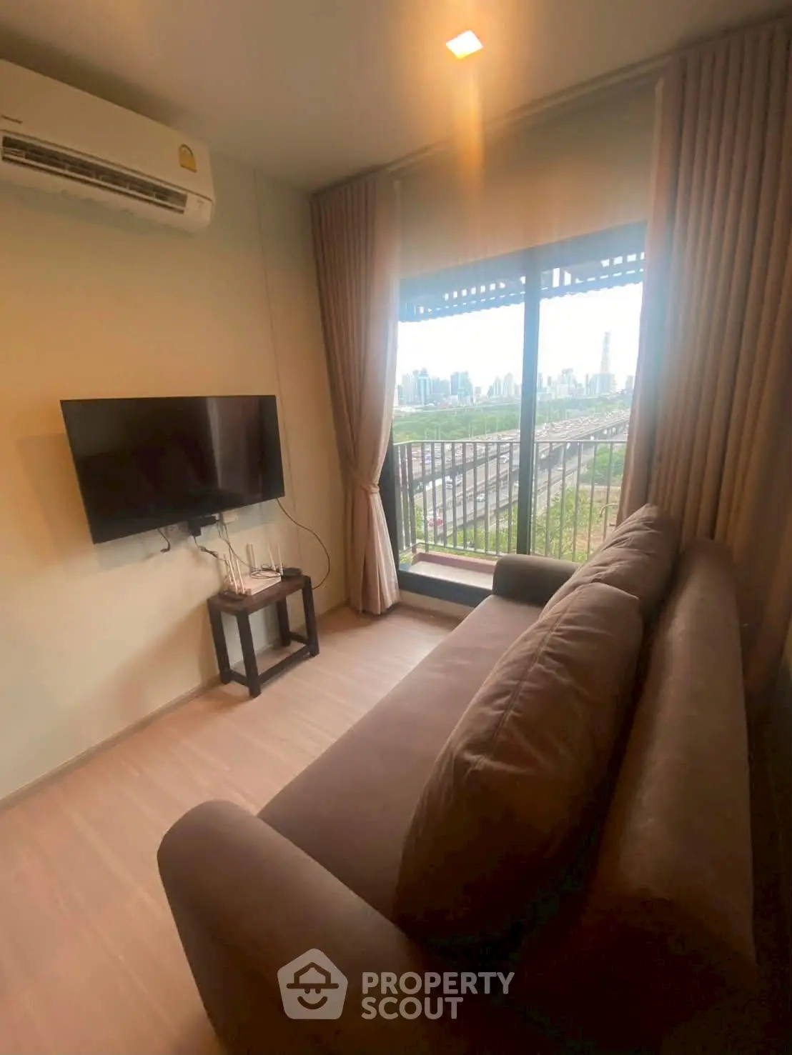 Cozy living room with city view, featuring a plush sofa and wall-mounted TV, perfect for relaxation.