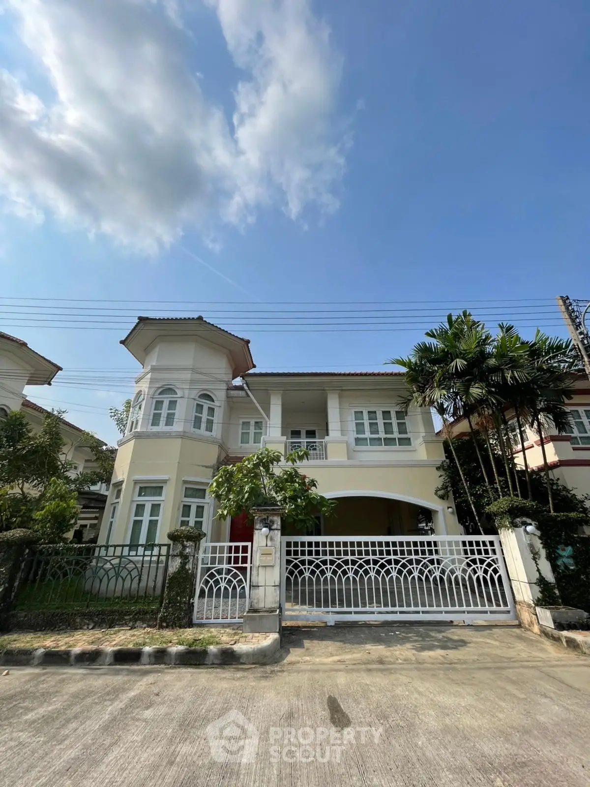 Charming two-story house with gated entrance and lush greenery in a serene neighborhood.