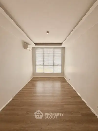 Spacious empty room with wooden flooring and large window, perfect for customization.