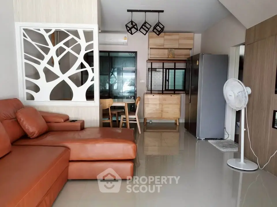 Modern living room with stylish decor and open kitchen layout, featuring leather sofa and contemporary lighting.