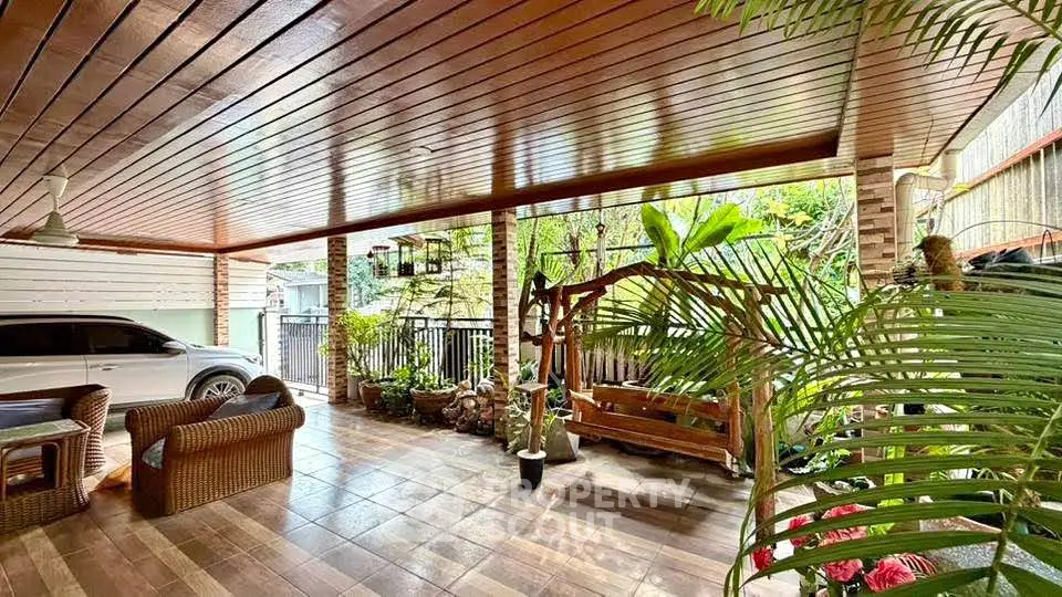 Spacious covered patio with wooden ceiling, wicker furniture, and lush garden view.