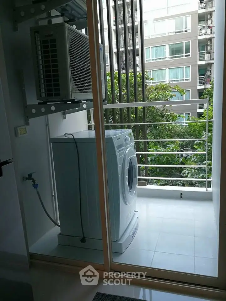 Modern apartment balcony with washing machine and air conditioning unit, overlooking urban view.