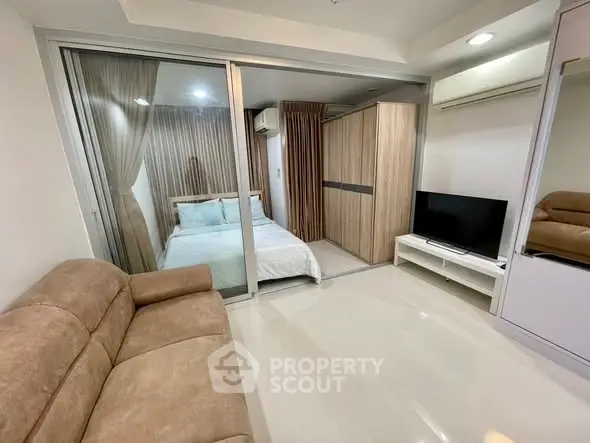 Modern apartment with cozy living room and glass-walled bedroom, featuring neutral tones and sleek furnishings.