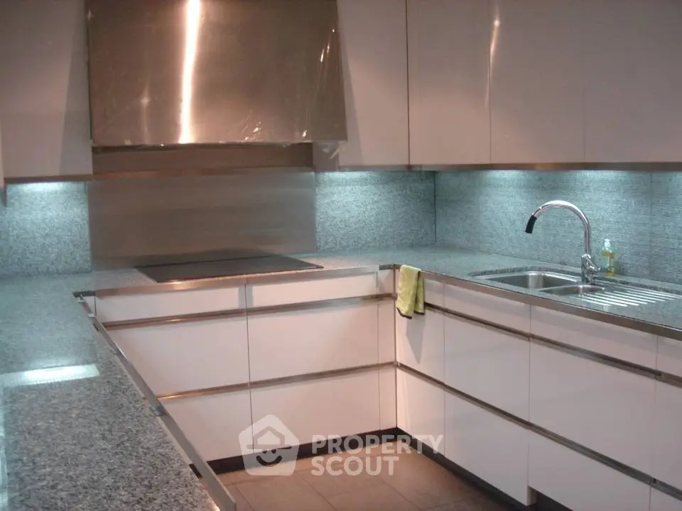 Modern kitchen with sleek white cabinets and granite countertops, featuring an integrated cooktop and stainless steel sink.