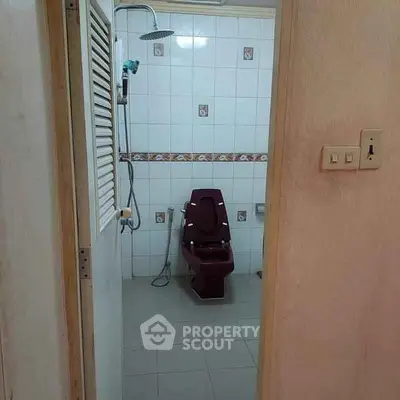 Unique bathroom with maroon toilet and shower in tiled setting.
