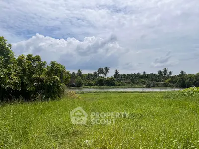 Scenic view of lush green field with trees and distant water body under a cloudy sky.
