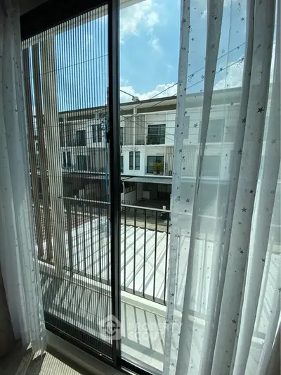 Bright balcony view with sheer curtains overlooking modern residential buildings.