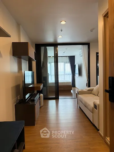 Modern living room with wooden flooring and cozy sofa leading to a bright bedroom.