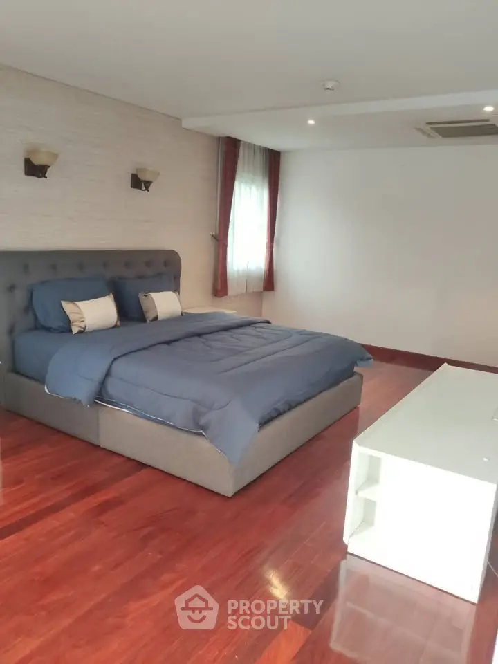 Spacious bedroom with elegant hardwood flooring and modern furnishings.