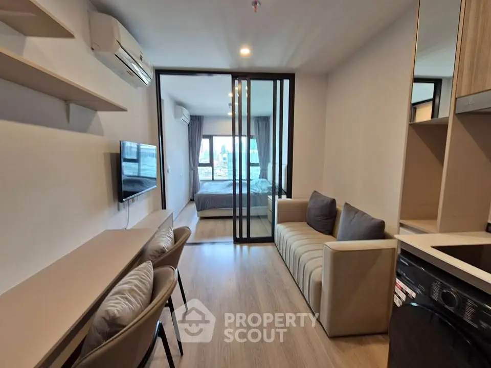 Modern apartment interior with open living room and bedroom, featuring sleek furniture and natural light.