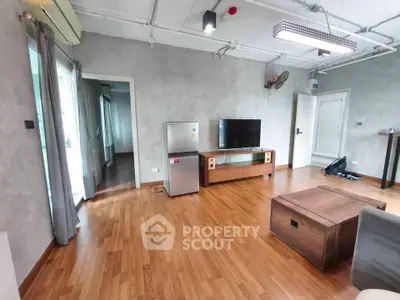 Spacious living room with modern decor and wooden flooring, featuring a TV and refrigerator.