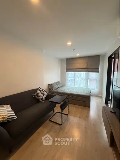Modern studio apartment with cozy living area and bed, featuring wooden flooring and large window.