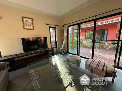 Cozy living room with glass table and TV, opening to a sunny patio with garden view.