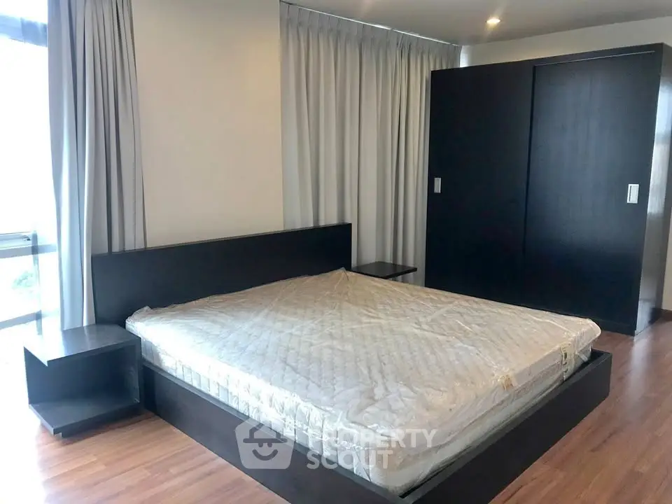 Spacious bedroom with modern dark wood furniture and large windows.