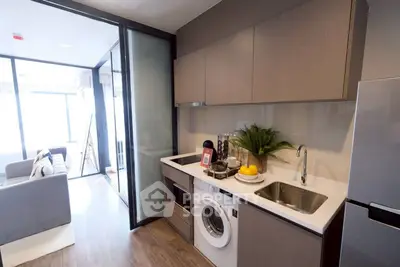 Modern kitchen with washing machine and sleek cabinetry in open layout apartment.