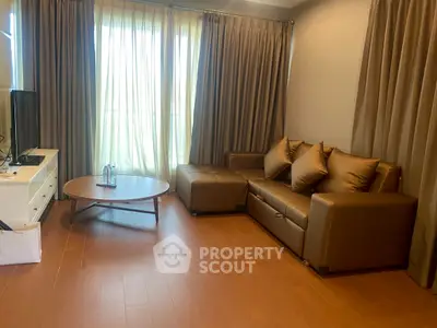 Cozy living room with brown leather sofa and natural light through large windows.