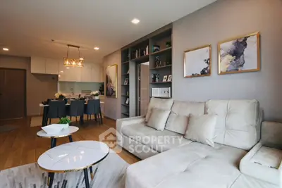 Modern living room with elegant decor and open kitchen layout, featuring stylish furniture and artwork.