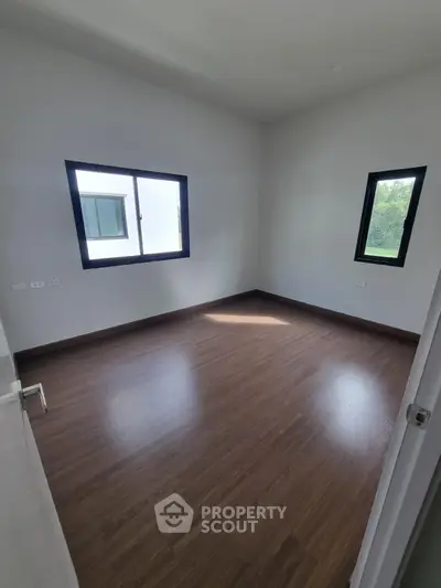 Spacious empty room with wooden flooring and large windows for natural light