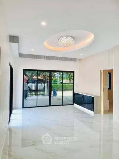 Spacious modern living room with elegant chandelier and large glass doors opening to a garden view.