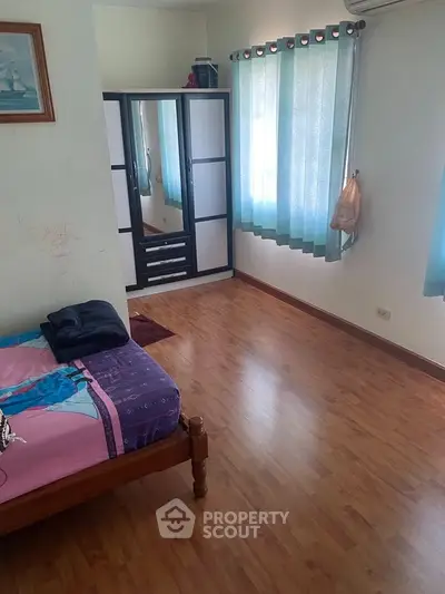 Spacious bedroom with wooden flooring and large window for natural light.