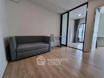 Modern living room with sleek gray sofa and glass partition leading to balcony.