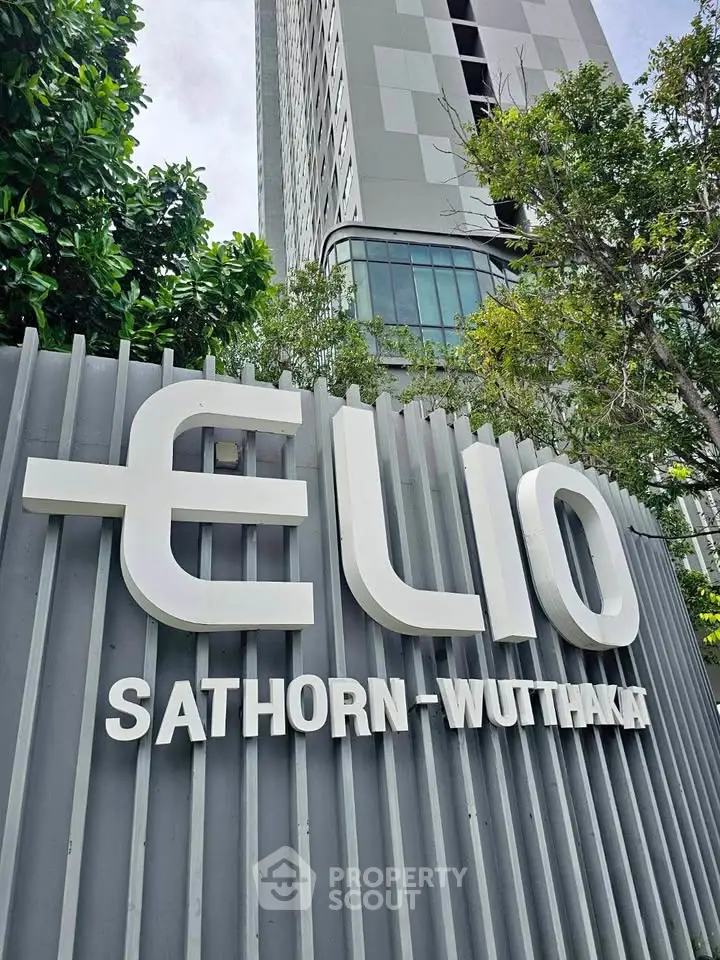 Modern high-rise building with Elio Sathorn-Wutthakat signage, surrounded by lush greenery.