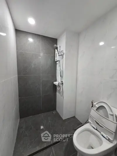 Modern bathroom with sleek gray and white tiles, featuring a shower and toilet.