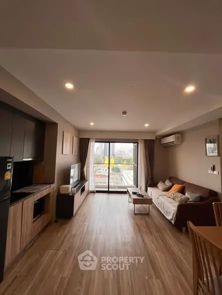 Spacious modern living room with large windows and city view, featuring cozy seating and sleek wooden flooring.