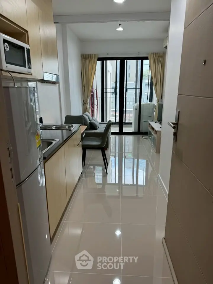 Modern apartment kitchen with sleek appliances and bright living area leading to a balcony.