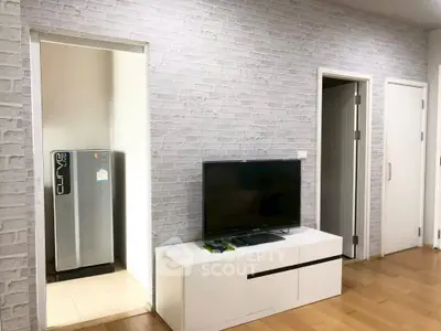 Modern living room with TV and fridge, featuring stylish brick wall design.