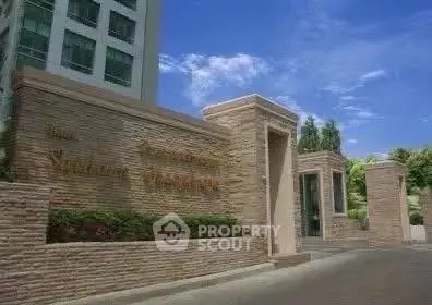 Elegant entrance of a modern residential building with stone facade and lush greenery.