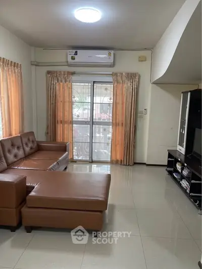 Spacious living room with modern brown leather sofa and large window for natural light.