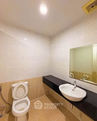 Modern bathroom with sleek fixtures and neutral tiles, featuring a wall-mounted sink and toilet.
