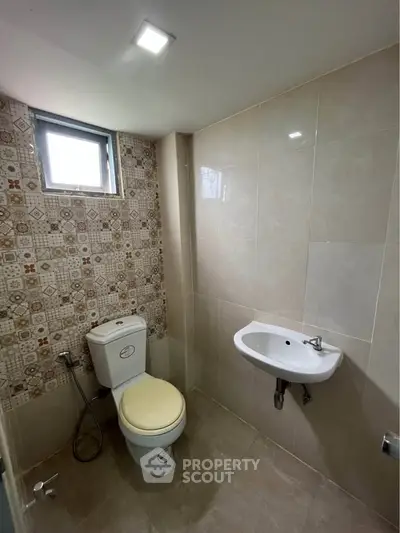 Modern bathroom with tiled walls and compact fixtures, featuring a window for natural light.
