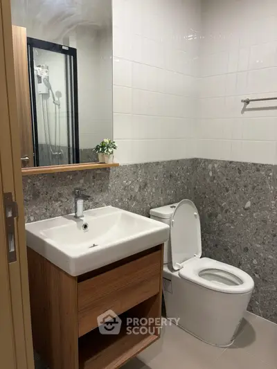 Modern bathroom with sleek sink and toilet, featuring elegant tile design and a touch of greenery.