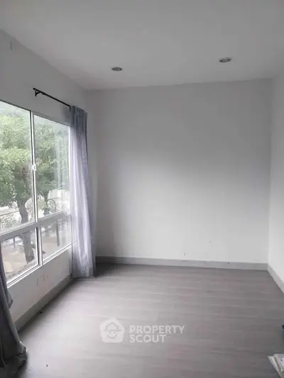 Bright empty room with large window and modern flooring, perfect for customization.