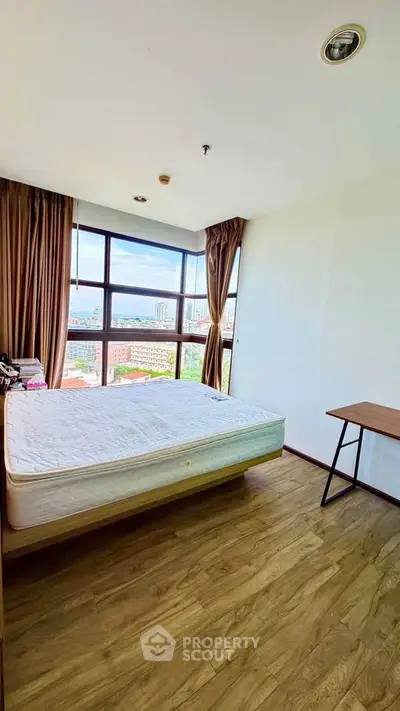 Bright bedroom with large windows offering stunning city views and wooden flooring.