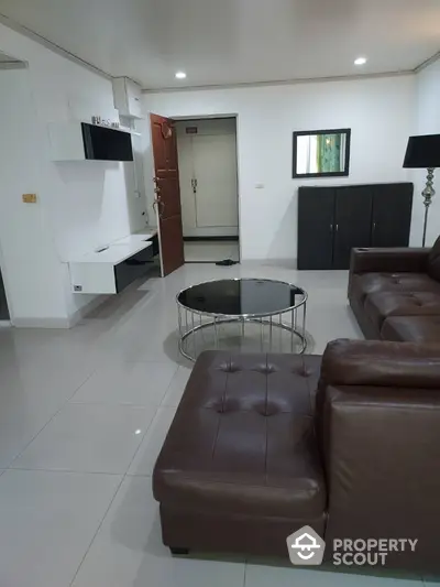 Spacious and modern living room with glossy tiled flooring, plush leather sofas, and sleek white entertainment unit, perfect for urban living.