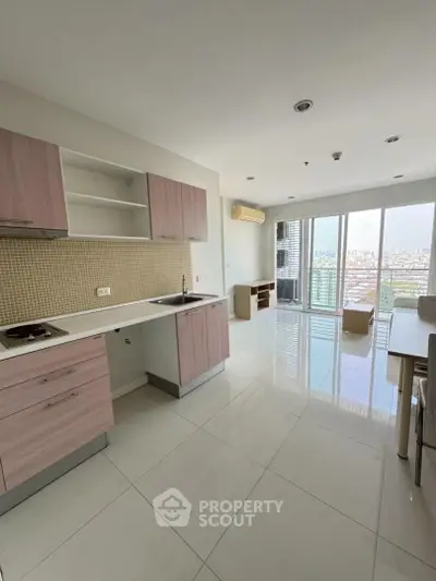 Modern open-plan kitchen and living area with city view, featuring sleek cabinetry and large windows.