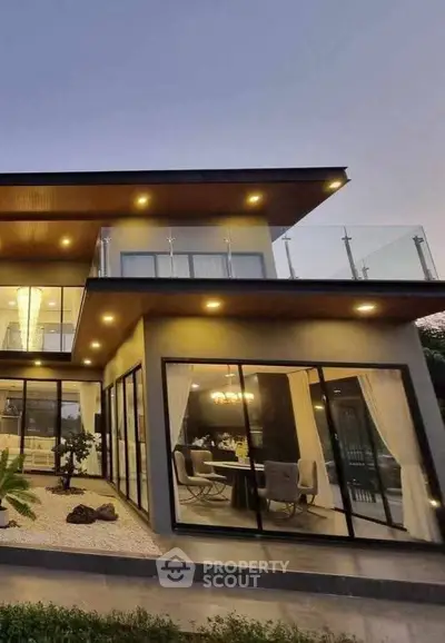Modern two-story house with large glass windows and elegant lighting at dusk.