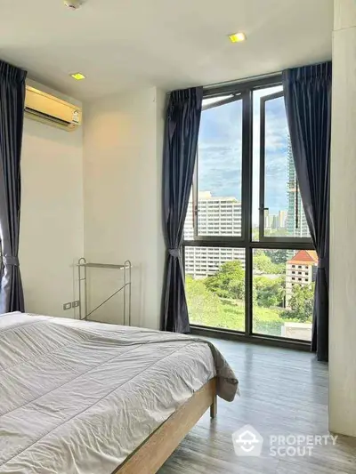 Bright bedroom with large windows offering a stunning city view, modern decor and air conditioning.