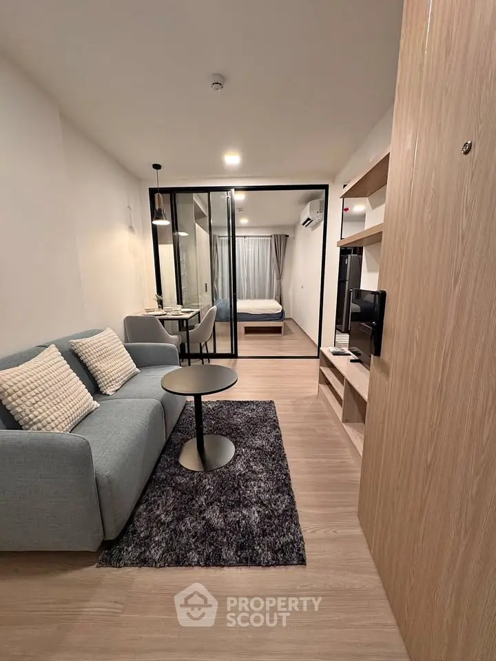 Modern studio apartment with cozy living area and stylish bedroom separated by glass partition.