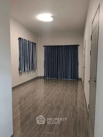 Spacious empty room with wooden flooring and blue curtains, ideal for customization.