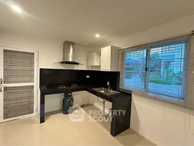 Modern kitchen with sleek black countertops and gas stove, featuring large window with garden view.